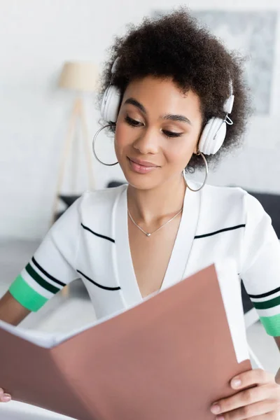 Heureuse femme afro-américaine dans les écouteurs sans fil regardant dossier — Photo de stock