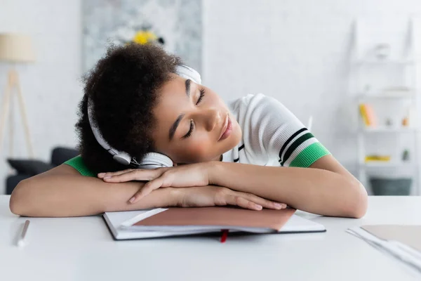 Mujer afroamericana cansada en auriculares inalámbricos durmiendo en el portátil - foto de stock