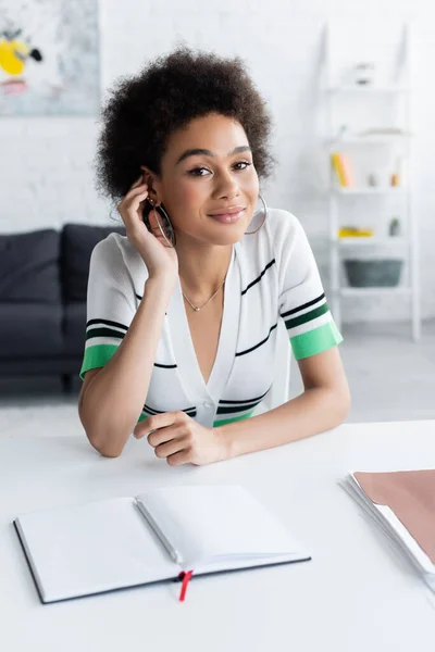 Joyeuse femme afro-américaine souriant près du carnet — Photo de stock