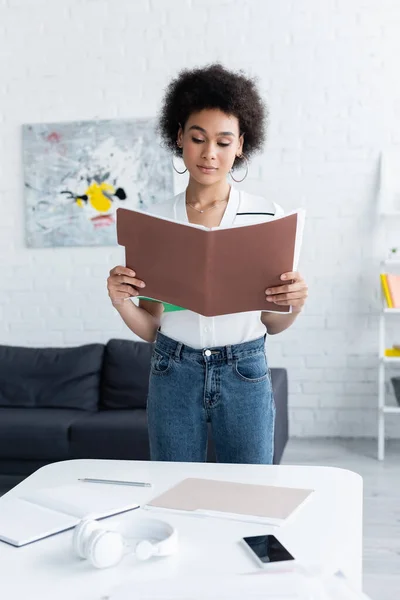 African american woman holding paper folder near smartphone and headphones at home — Stock Photo