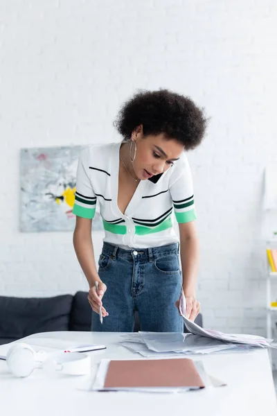 Mujer afroamericana hablando por celular y sosteniendo documentos en casa - foto de stock