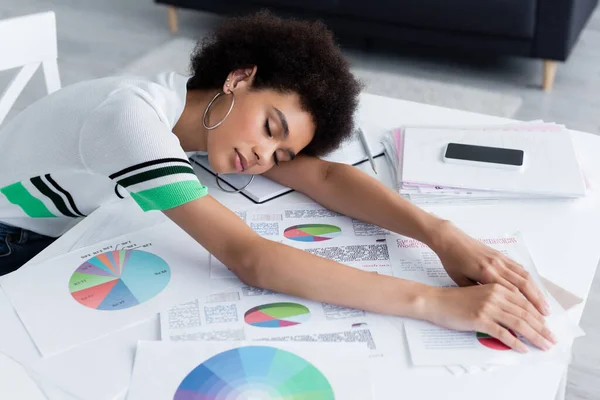 Young african american woman lying near papers with charts and cellphone on table — Stock Photo