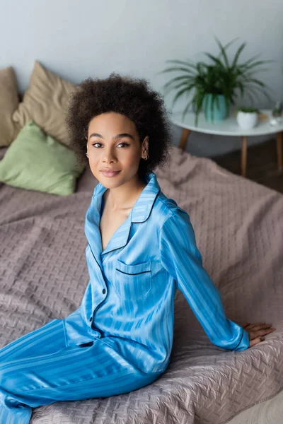 Junge Afroamerikanerin im Pyjama blickt auf Kamera auf Bett — Stockfoto