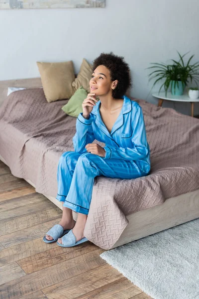 Dreamy african american woman sitting on bed at home — Stock Photo