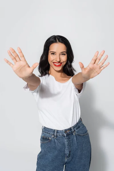Smiling brunette woman in white t-shirt posing with outstretched hands on grey — Stock Photo
