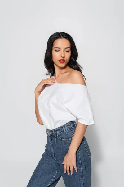 Femme sensuelle avec des lèvres rouges posant en t-shirt blanc avec épaule nue sur gris — Photo de stock