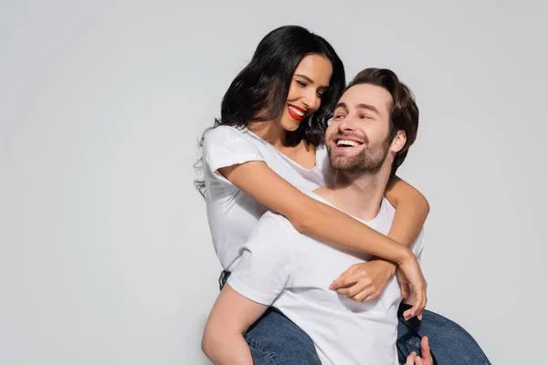 Jovem homem piggybacking jovem mulher abraçando-o isolado no cinza — Fotografia de Stock