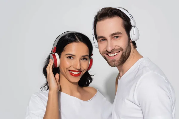 Alegre jovem casal em fones de ouvido olhando para a câmera enquanto ouve música em cinza — Fotografia de Stock