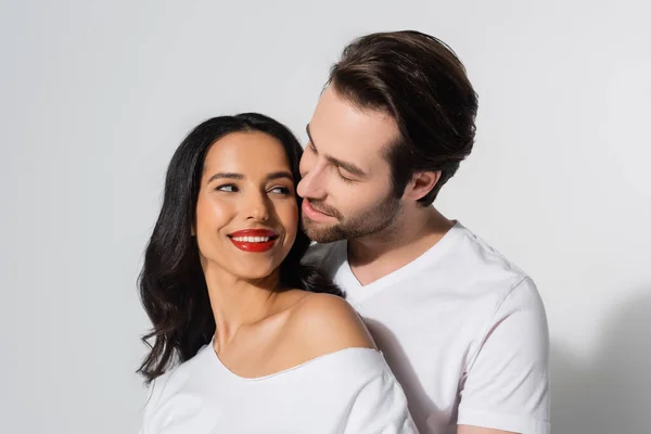 Jovem morena mulher em branco t-shirt sorrindo perto de jovem no cinza — Fotografia de Stock