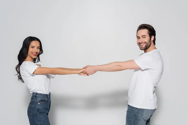 Couple gai en t-shirts blancs regardant la caméra tout en tenant la main sur le gris — Photo de stock