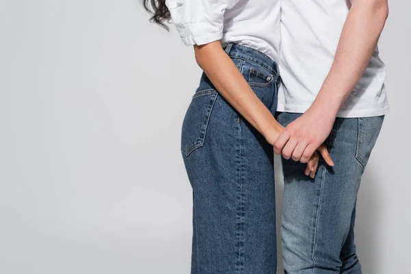 Visión parcial del hombre y la mujer en jeans tomados de la mano en gris - foto de stock