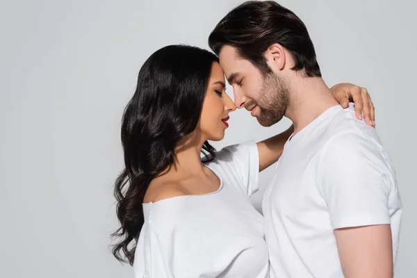 Side view of brunette woman embracing man while standing face to face with closed eyes isolated on grey — Stock Photo