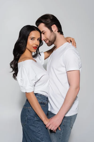 Sexy brunette woman looking at camera while holding hands with young man on grey — Stock Photo