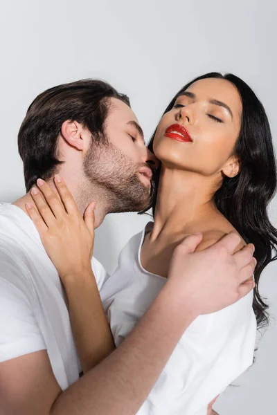 Young man kissing neck of passionate brunette woman with closed eyes on grey — Stock Photo