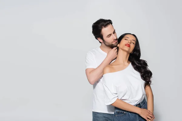 Hombre joven tocando cuello de mujer apasionada con los ojos cerrados aislados en gris - foto de stock