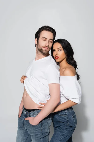 Sexy woman looking at camera while taking t-shirt off young man on grey — Stock Photo