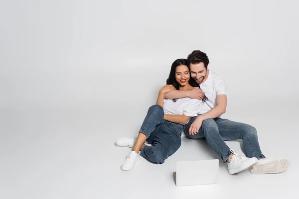 Couple heureux en vêtements décontractés regarder film sur ordinateur portable sur gris — Photo de stock