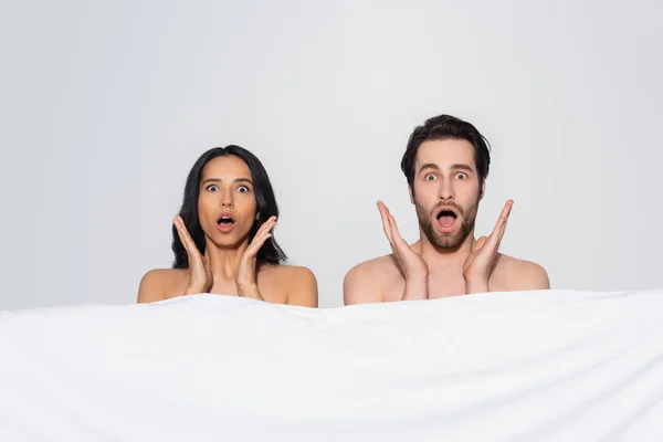 Shocked couple with open mouths looking at camera near white blanket isolated on grey — Stock Photo