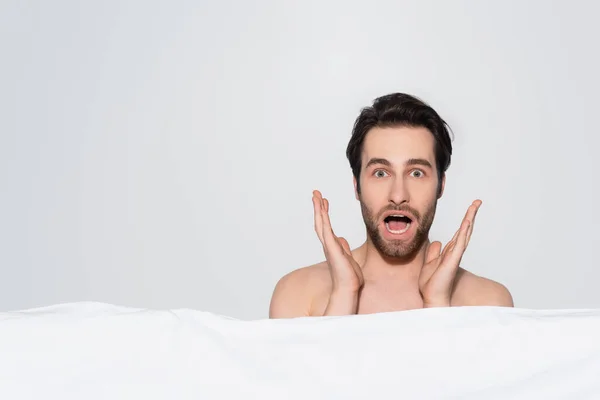 Jeune homme choqué avec bouche ouverte regardant caméra près couverture blanche isolé sur gris — Photo de stock