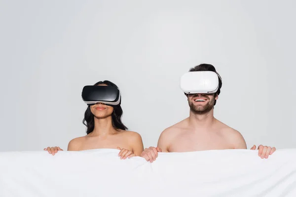 Happy couple with white blanket gaming in vr headsets isolated on grey — Stock Photo