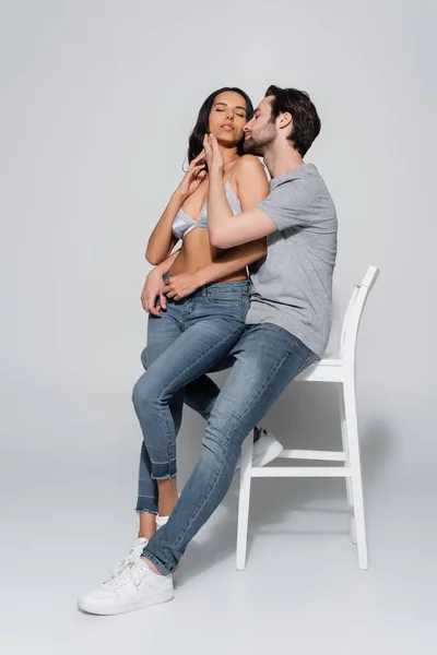 Vista completa de la joven pareja apasionada abrazando mientras está sentado en la silla en gris - foto de stock