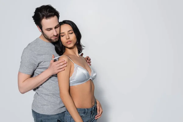 Man in t-shirt touching satin bra of young passionate woman on grey — Stock Photo