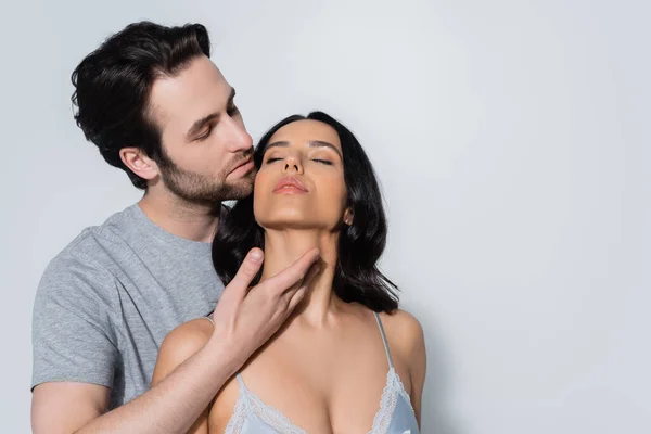Young man in t-shirt seducing sexy woman in bra while touching her neck on grey — Stock Photo