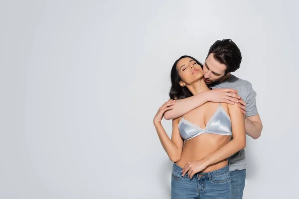 Sexy woman in jeans and bra near brunette man hugging her on grey — Stock Photo