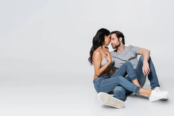 Sexy brunette woman in jeans and satin bra seducing young man while sitting on grey — Stock Photo