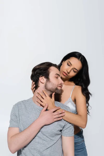 Passionate brunette woman in bra seducing young man while hugging him isolated on grey — Stock Photo