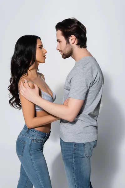 Side view of brunette woman in bra embracing man in t-shirt on grey — Stock Photo
