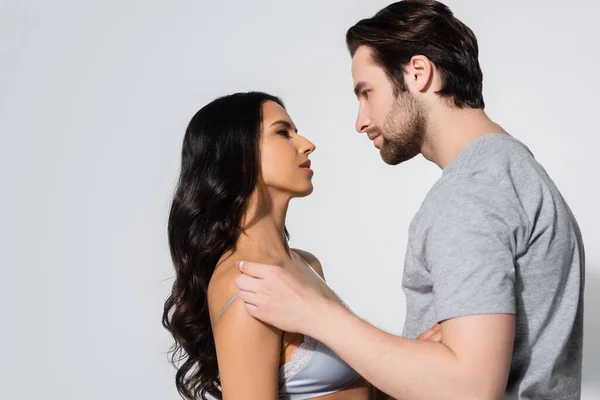 Vista lateral do homem em t-shirt e mulher em sutiã olhando uns para os outros isolado em cinza — Fotografia de Stock