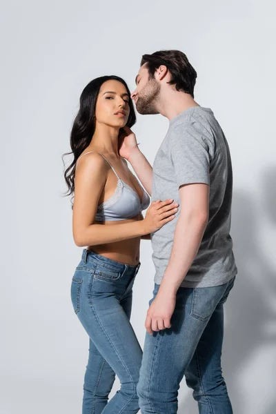 Man in t-shirt seducing woman in jeans and bra on grey — Stock Photo