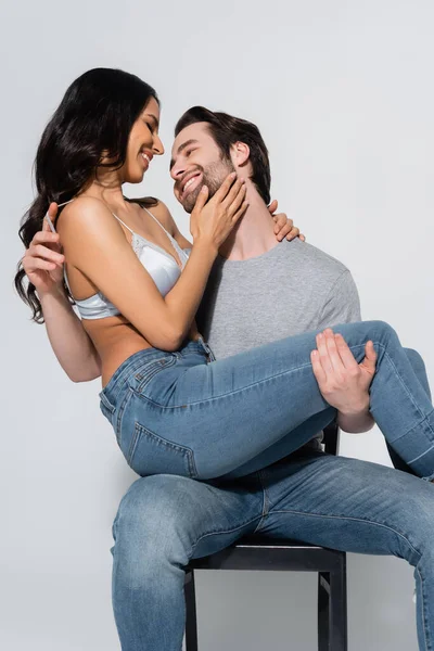 Happy man holding sexy woman in jeans and bra on grey — Stock Photo