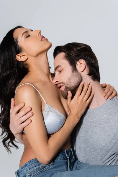 Uomo ad occhi chiusi che abbraccia donna in reggiseno di raso isolato su grigio — Foto stock