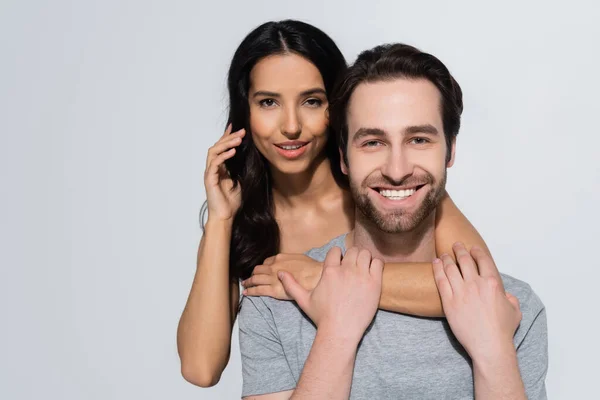 Pretty brunette woman looking at camera while hugging bearded man in t-shirt  isolated on grey — Stock Photo