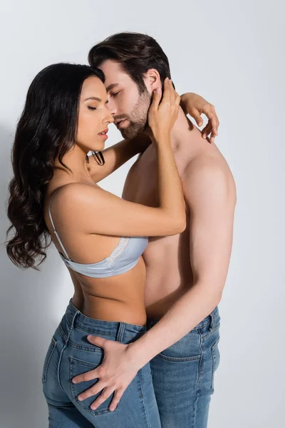 Sexy shirtless man and seductive woman in jeans and bra embracing on grey — Stock Photo