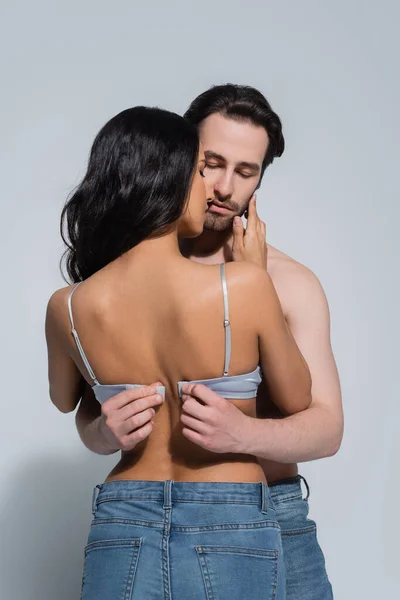 Young man with closed eyes unfastening bra on girlfriend on grey — Stock Photo