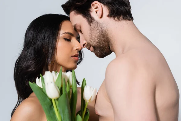 Pareja joven con los ojos cerrados de pie cerca de tulipanes aislados en gris - foto de stock