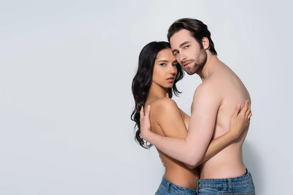 Sensual couple in jeans only embracing and looking at camera on grey — Stock Photo