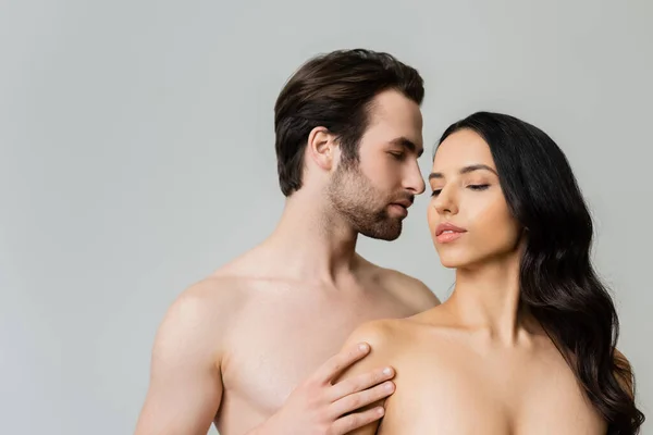 Young shirtless man touching nude brunette woman isolated on grey — Stock Photo