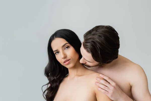 Молодой человек целует шею обнаженной женщины, смотрящей в камеру, изолированную от серых — стоковое фото