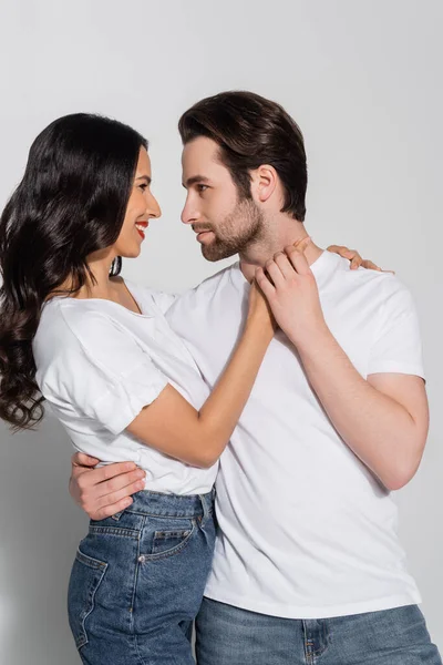 Молодая пара в белых футболках, смотрящая друг на друга, танцуя на сером — стоковое фото