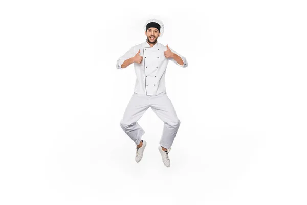 Amazed chef in hat and uniform jumping and showing thumbs up isolated on white — Stock Photo