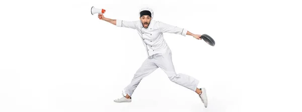 Chef surpris en chapeau et uniforme lévitant tout en tenant poêle à frire et mégaphone isolé sur blanc, bannière — Photo de stock