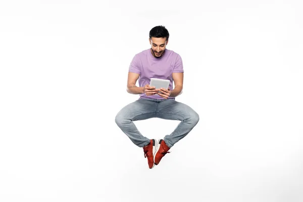 Homem feliz em jeans e camiseta roxa levitando ao usar tablet digital em branco — Fotografia de Stock