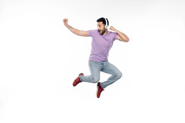 Verblüffter und tätowierter Mann mit kabellosen Kopfhörern schwebt auf weißem Grund — Stockfoto