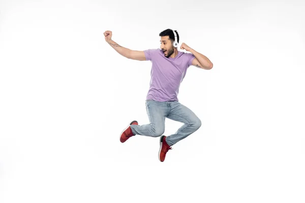 Hombre sorprendido y tatuado en auriculares inalámbricos levitando sobre blanco - foto de stock