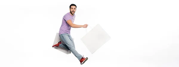 Happy man in jeans and purple t-shirt levitating with shopping bags on white, banner — Stock Photo