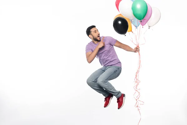 Glücklicher Mann springt und zeigt auf bunte Luftballons auf weißem Grund — Stockfoto